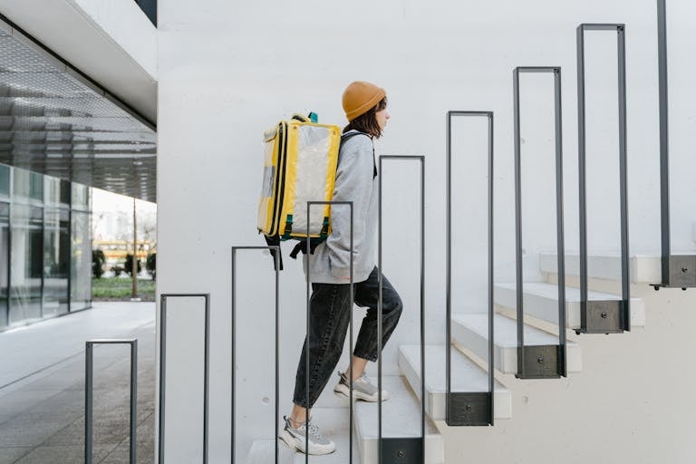 A female courier ascends stairs in an urban setting with a thermal delivery backpack.