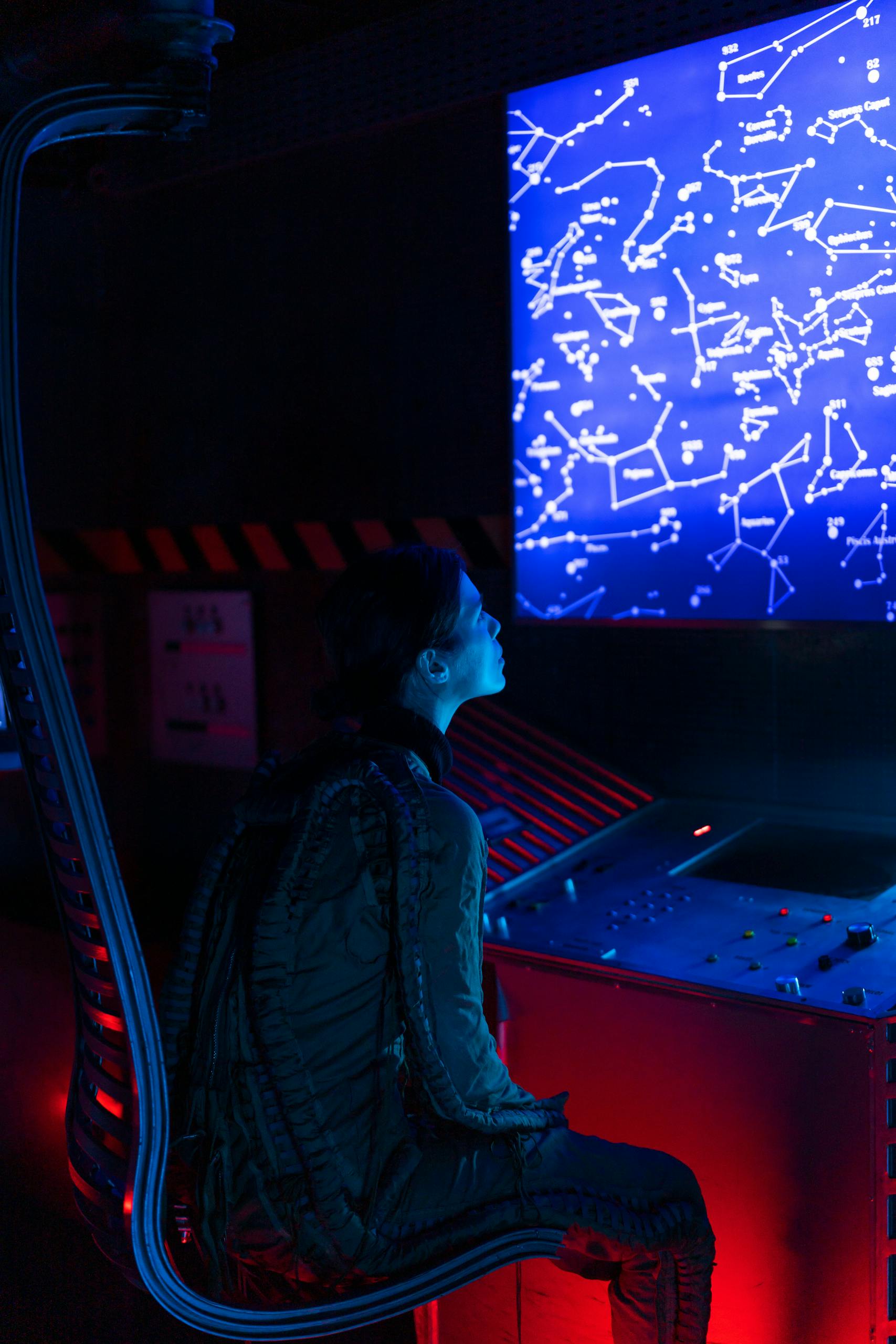A woman in a space suit studies a futuristic control panel displaying star constellations.