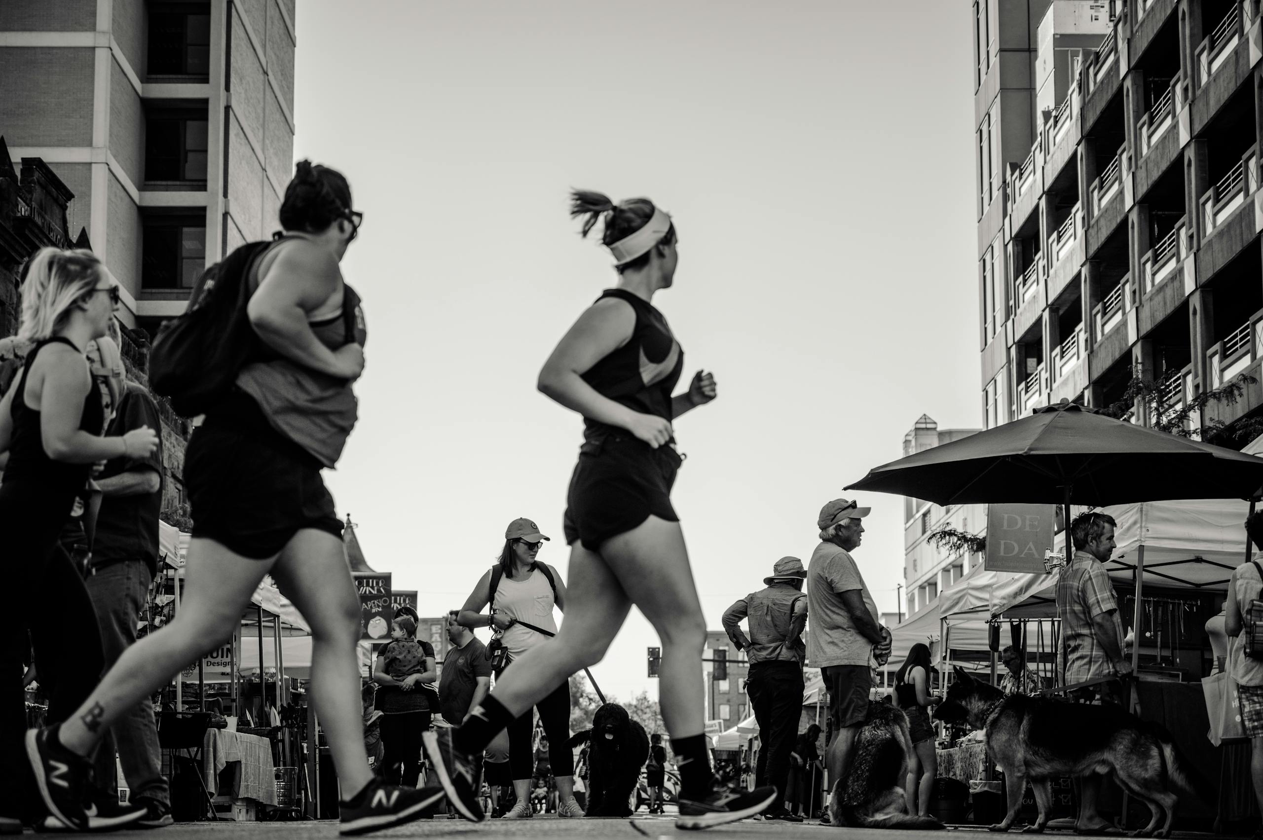 Black and white photo of people jogging and walking in a lively city street.