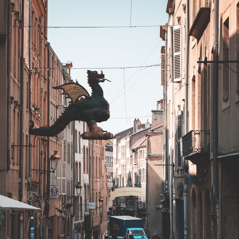 Sculpture of Graoully hanging in narrow avenue between residential buildings against cloudless sky on street of Metz in city of France