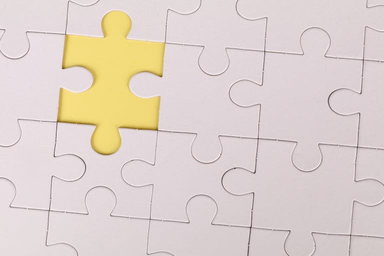 Close-up of a white jigsaw puzzle with a single yellow piece missing, symbolizing incompleteness.