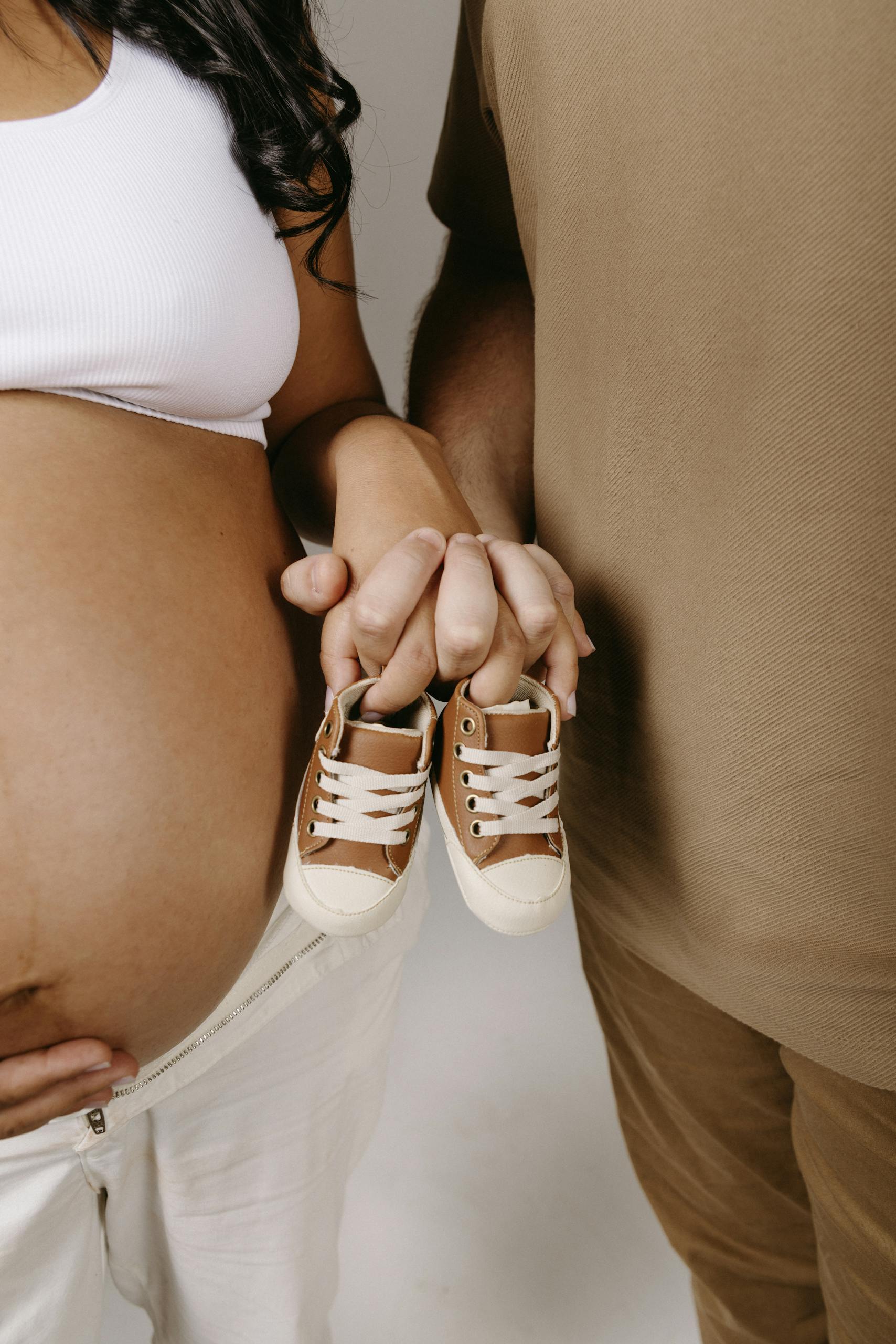 Expectant couple holding tiny brown baby shoes, symbolizing upcoming parenthood.